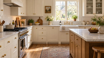 Traditional kitchen with cream shaker cabinets, a warm wood island, brass cabinet knobs, marble-look countertops, and natural daylight.