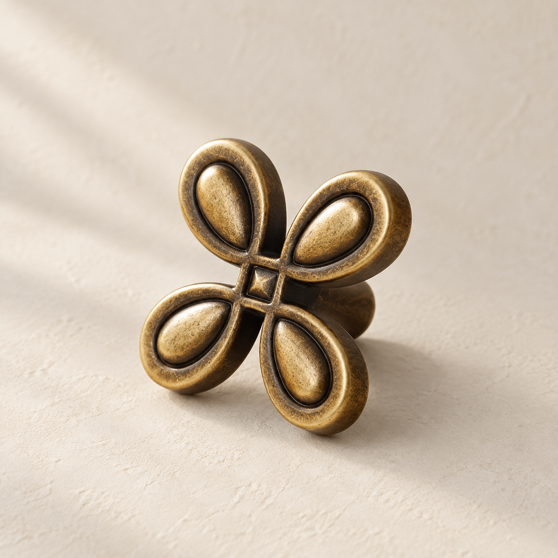 Solid Brass Four-Leaf Cabinet Knob — Antique Brass on a warm ivory background