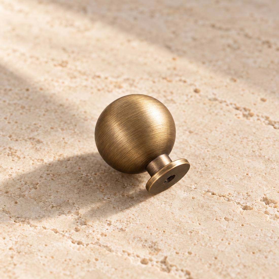 Antique Brass Round Cabinet Knob — Solid Brass on warm ivory stone