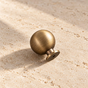 Antique Brass Round Cabinet Knob — Solid Brass on warm ivory stone