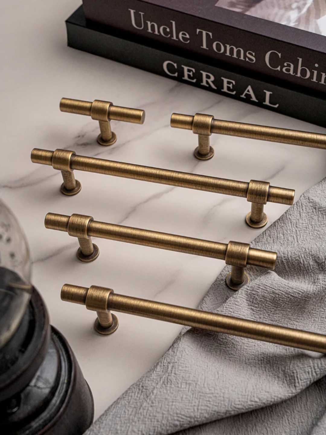 Set of gold cabinet handles on a marble surface with a book titled 'Uncle Tom's Cabin' in the background.