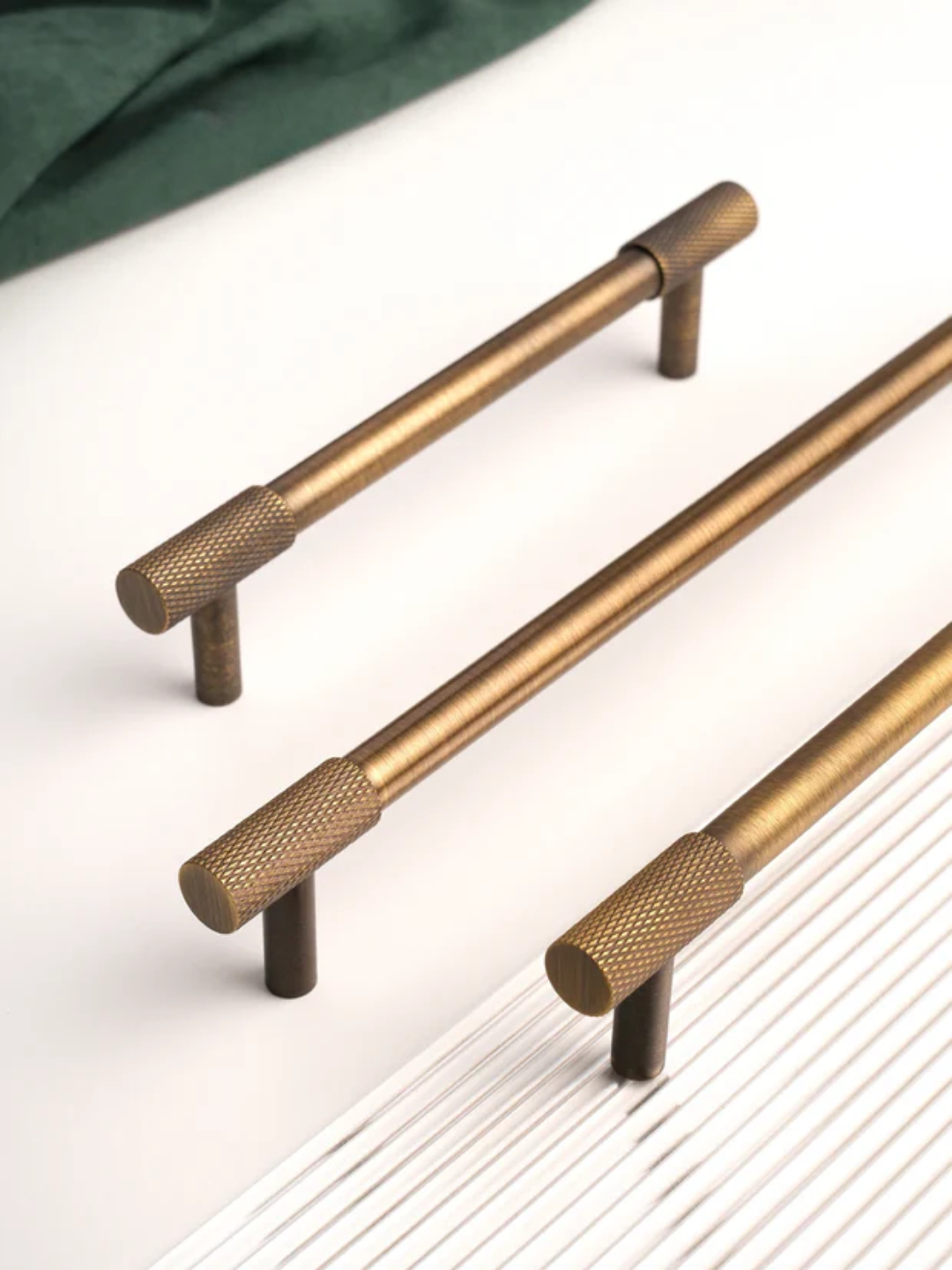 Three brass cabinet handles on a white surface with a green fabric background