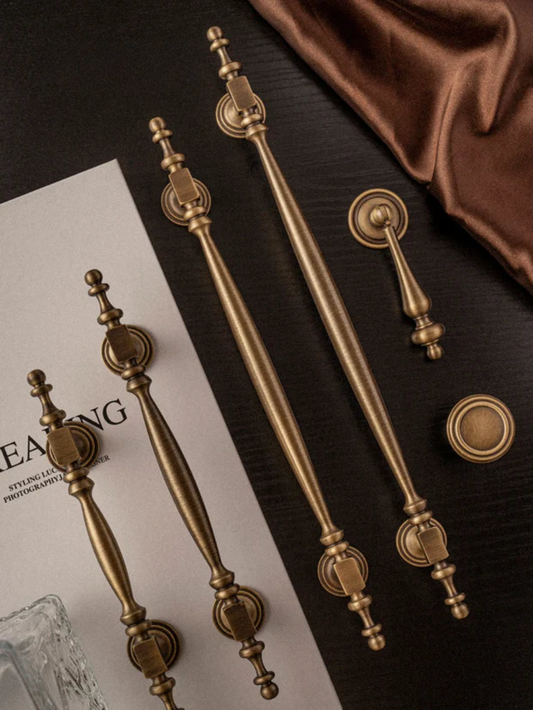 Set of decorative brass handles on a dark surface with a brown fabric background.
