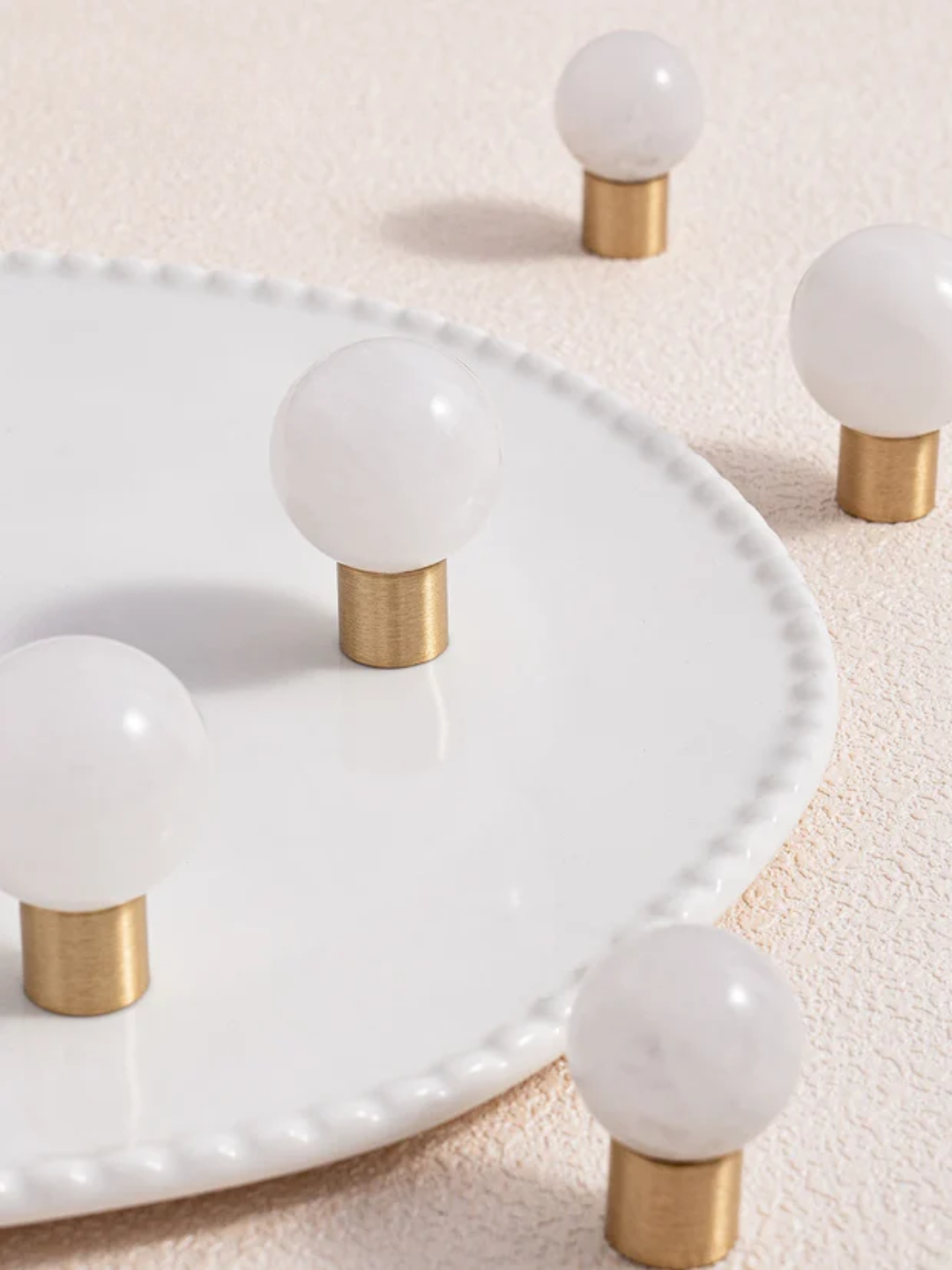 Decorative items with white spherical tops and gold cylindrical bases on a textured surface.