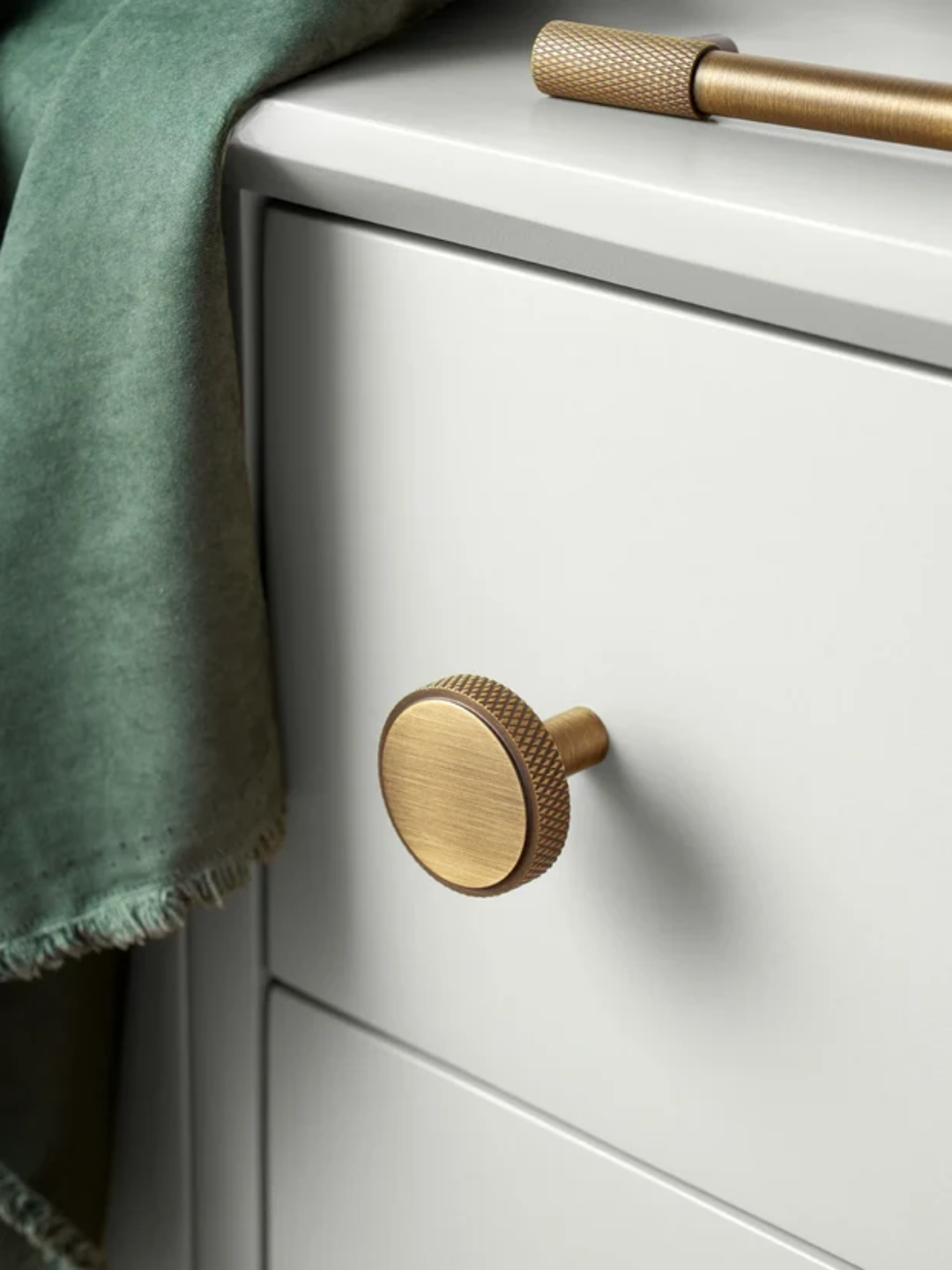 Close-up of a white cabinet with gold knobs and a green towel.