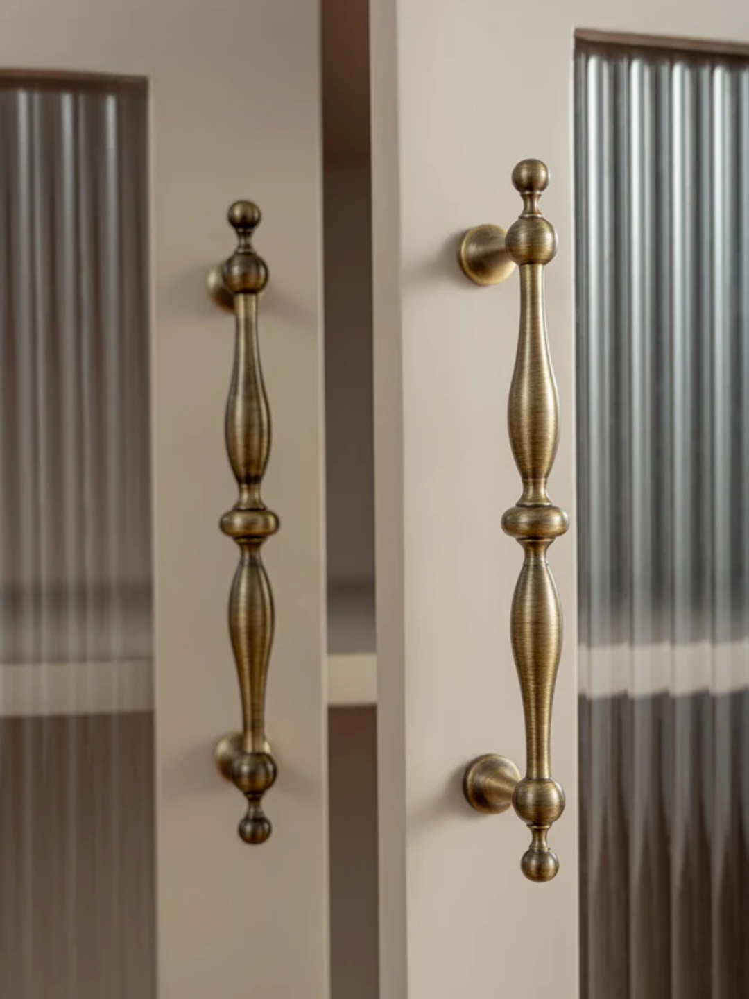 Pair of gold door handles on a glass door with a neutral background