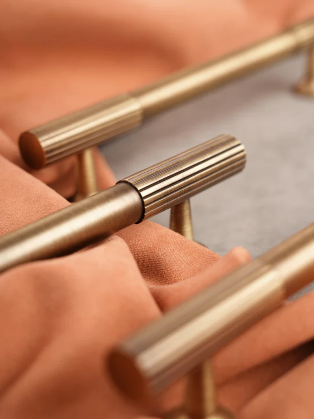 Close-up of gold metal handles on a piece of furniture with a soft pink background.
