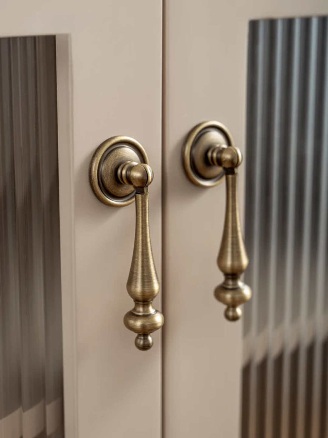 Close-up of two brass cabinet handles on a beige door.