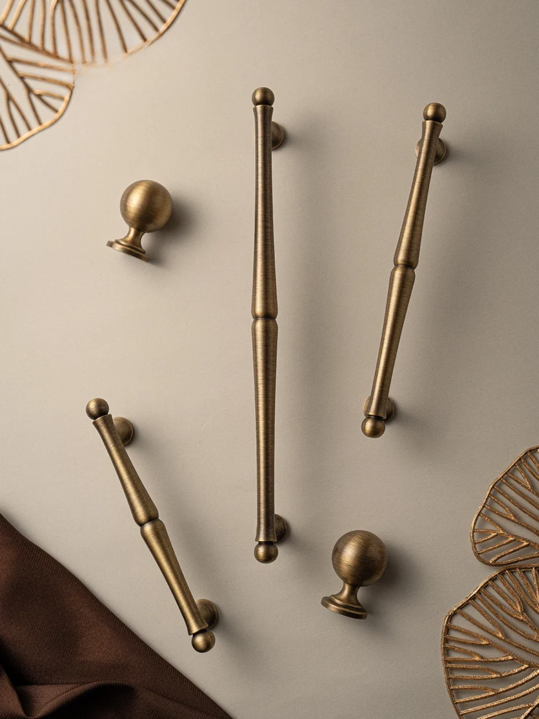 Set of bronze cabinet handles and knobs on a beige surface with decorative elements.
