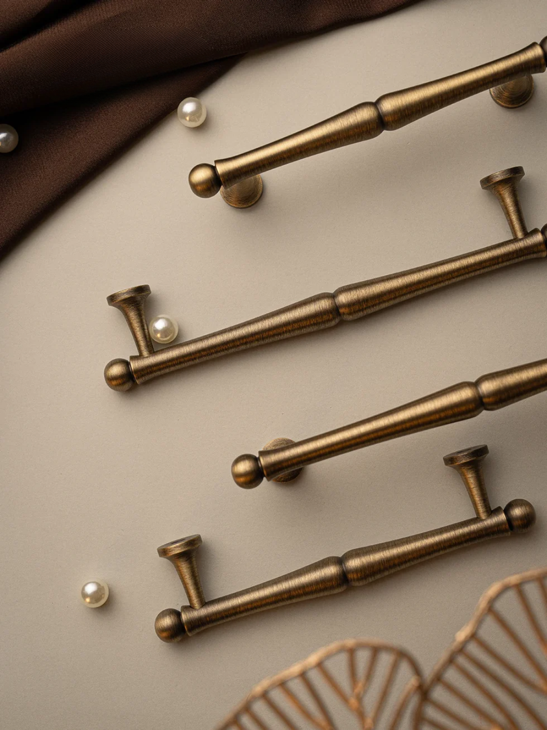 Bronze cabinet handles on a beige surface with pearls and fabric in the background