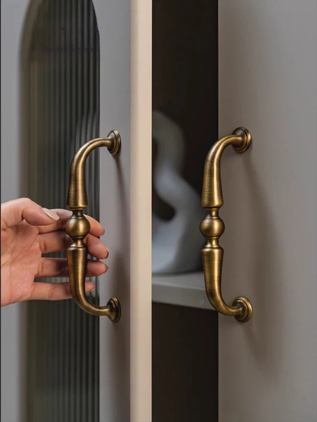 Hand opening a door with gold handles.