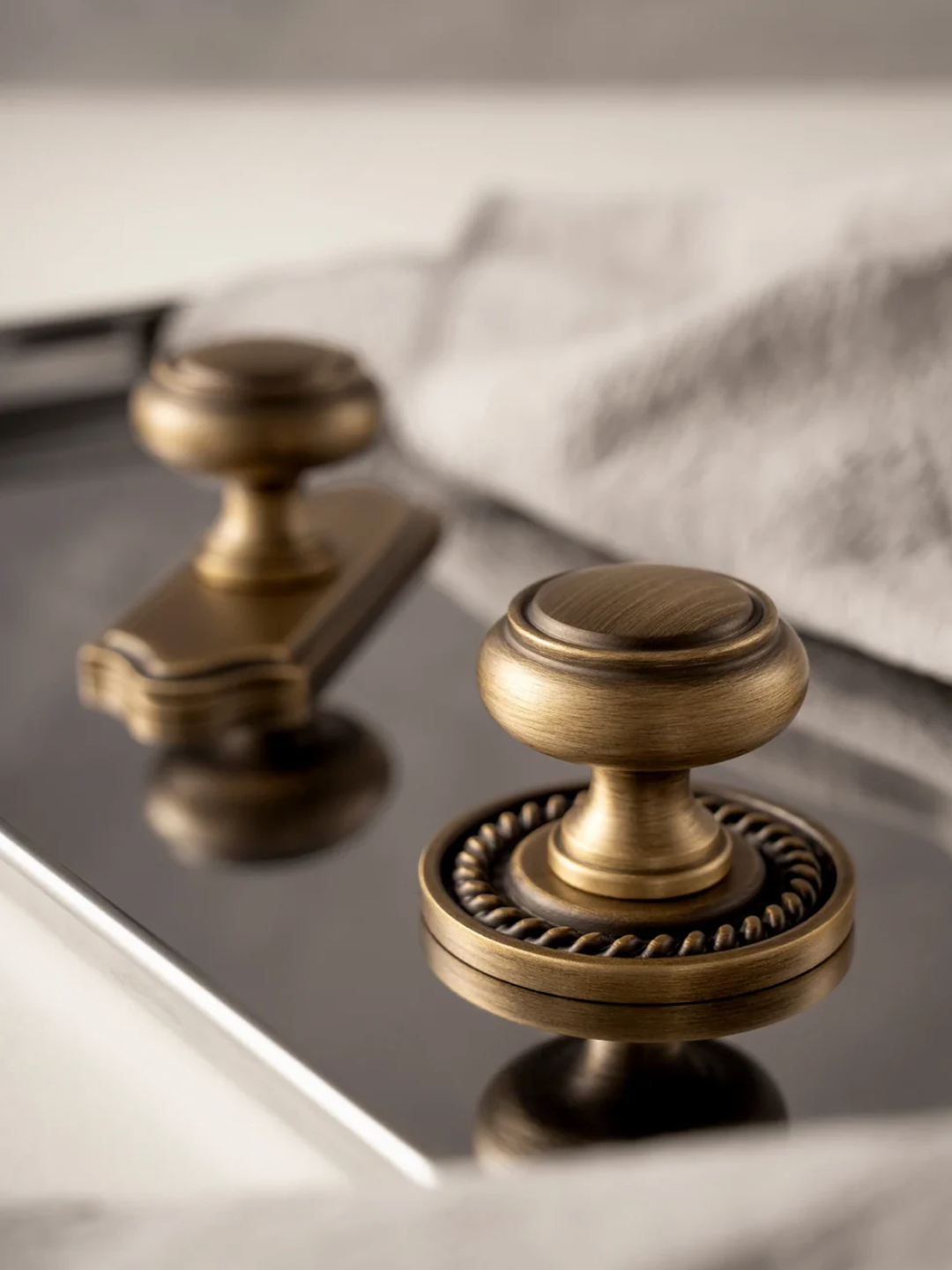 Two bronze cabinet knobs on a reflective surface with a white cloth in the background