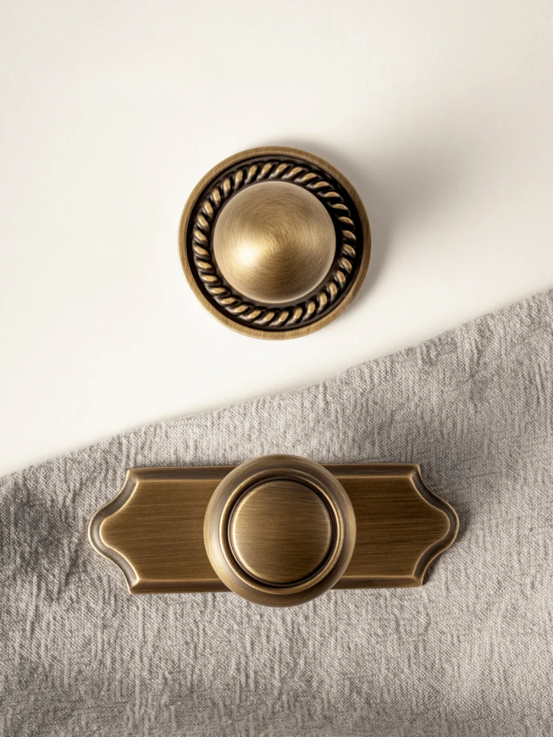 Two brass cabinet knobs on a textured surface with a white background