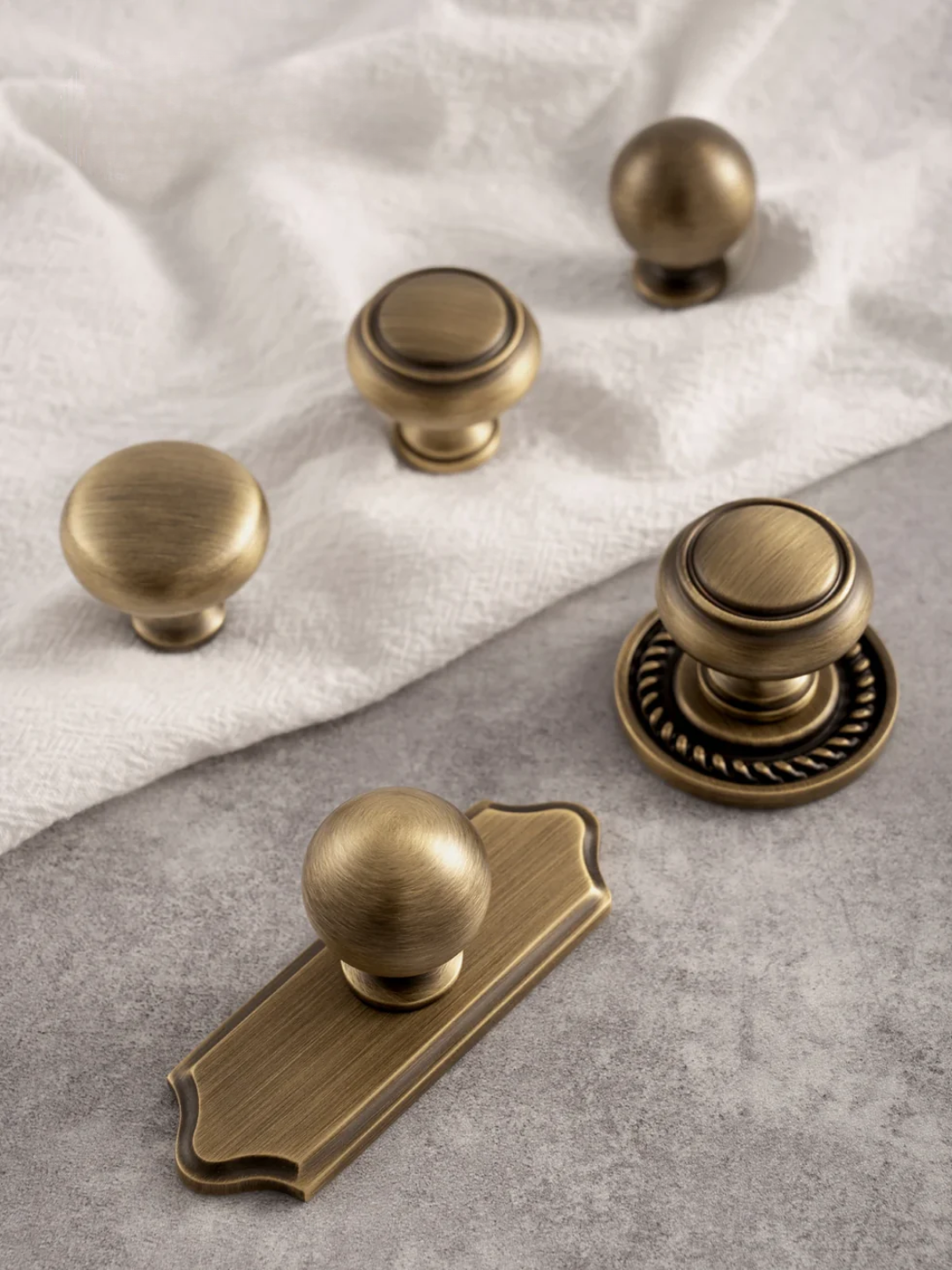 Collection of brass cabinet knobs and handles on a textured surface