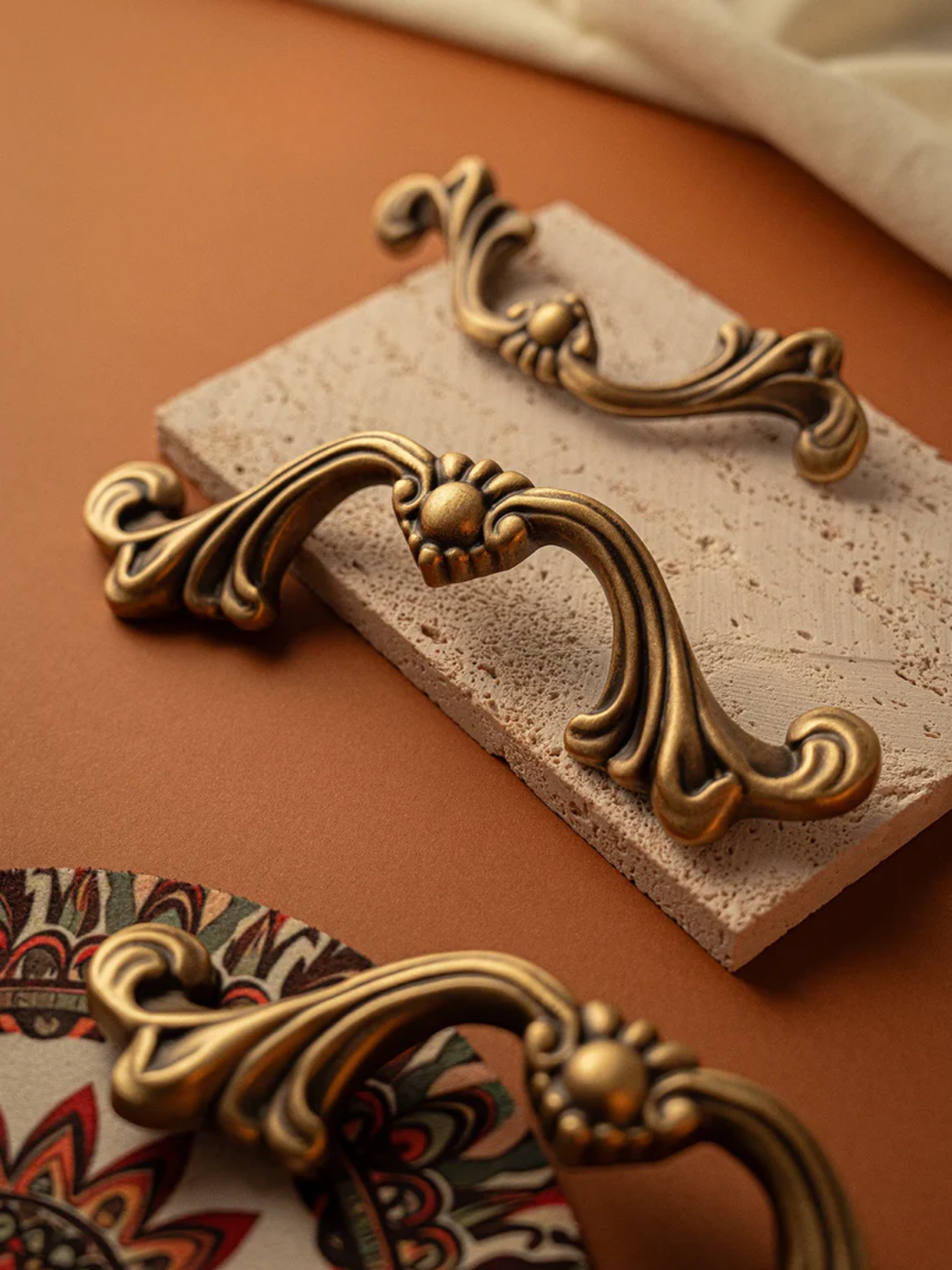 Set of decorative brass cabinet knobs on a brown surface with a patterned fabric background.