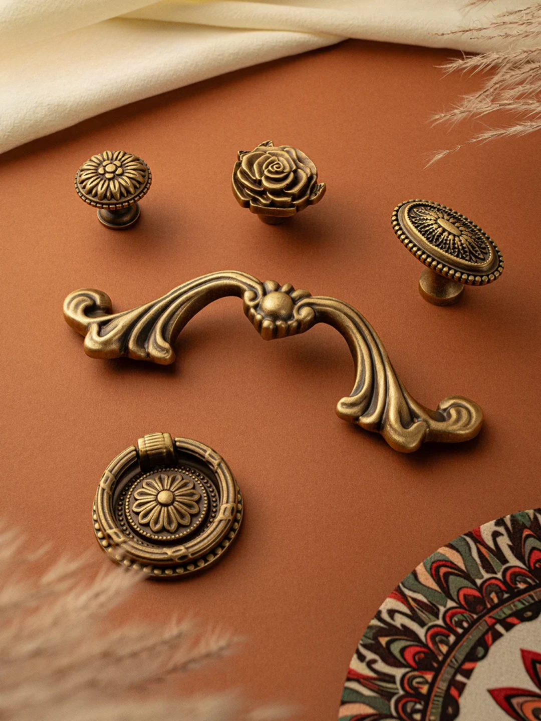 Set of decorative brass cabinet knobs on a brown surface with a patterned fabric background.