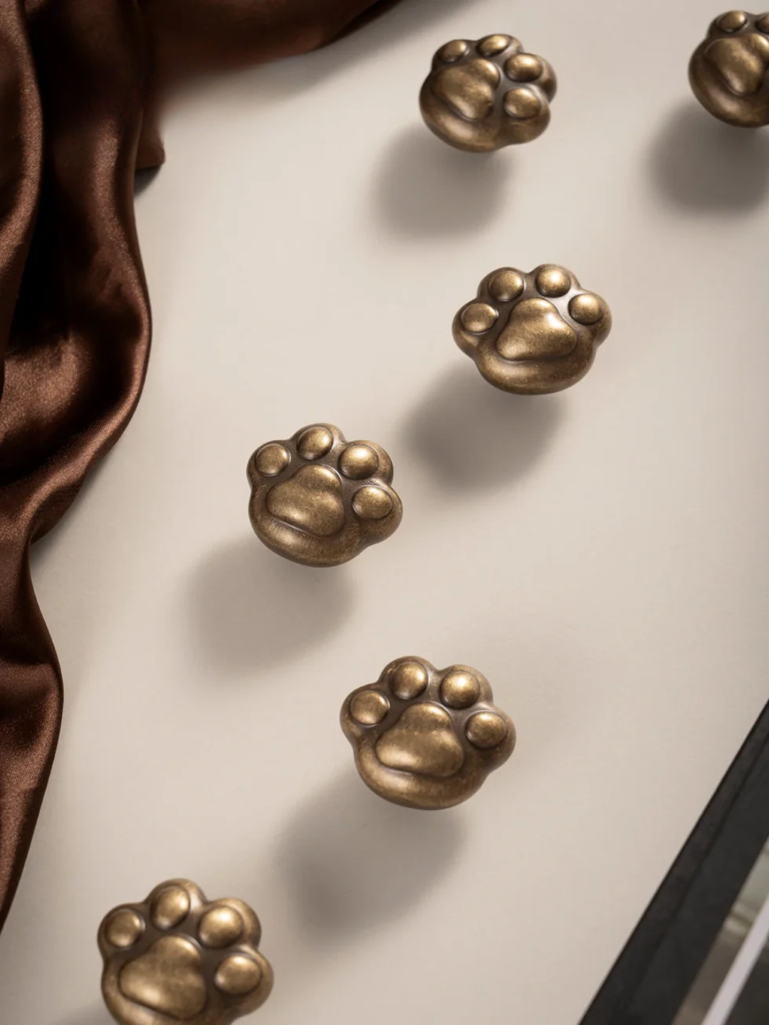 Bronze paw-shaped objects on a reflective surface with a brown fabric background