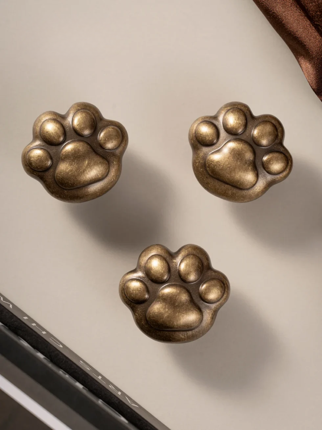 Three bronze paw-shaped knobs on a white surface