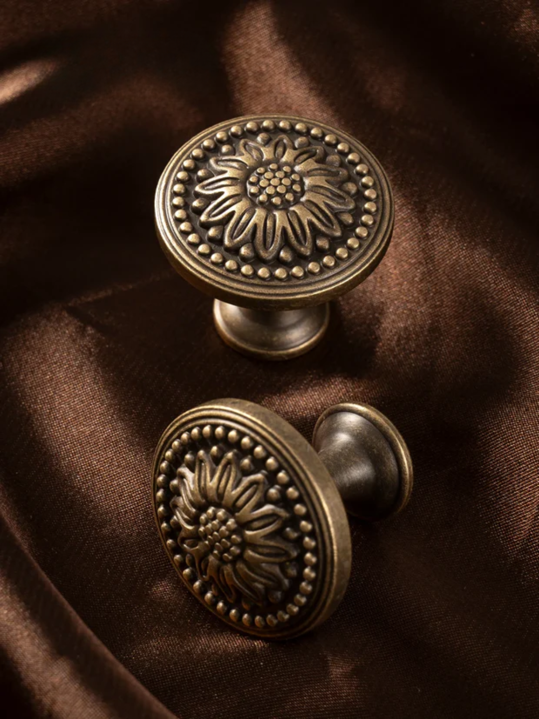 Two ornate bronze cabinet knobs on a brown fabric background