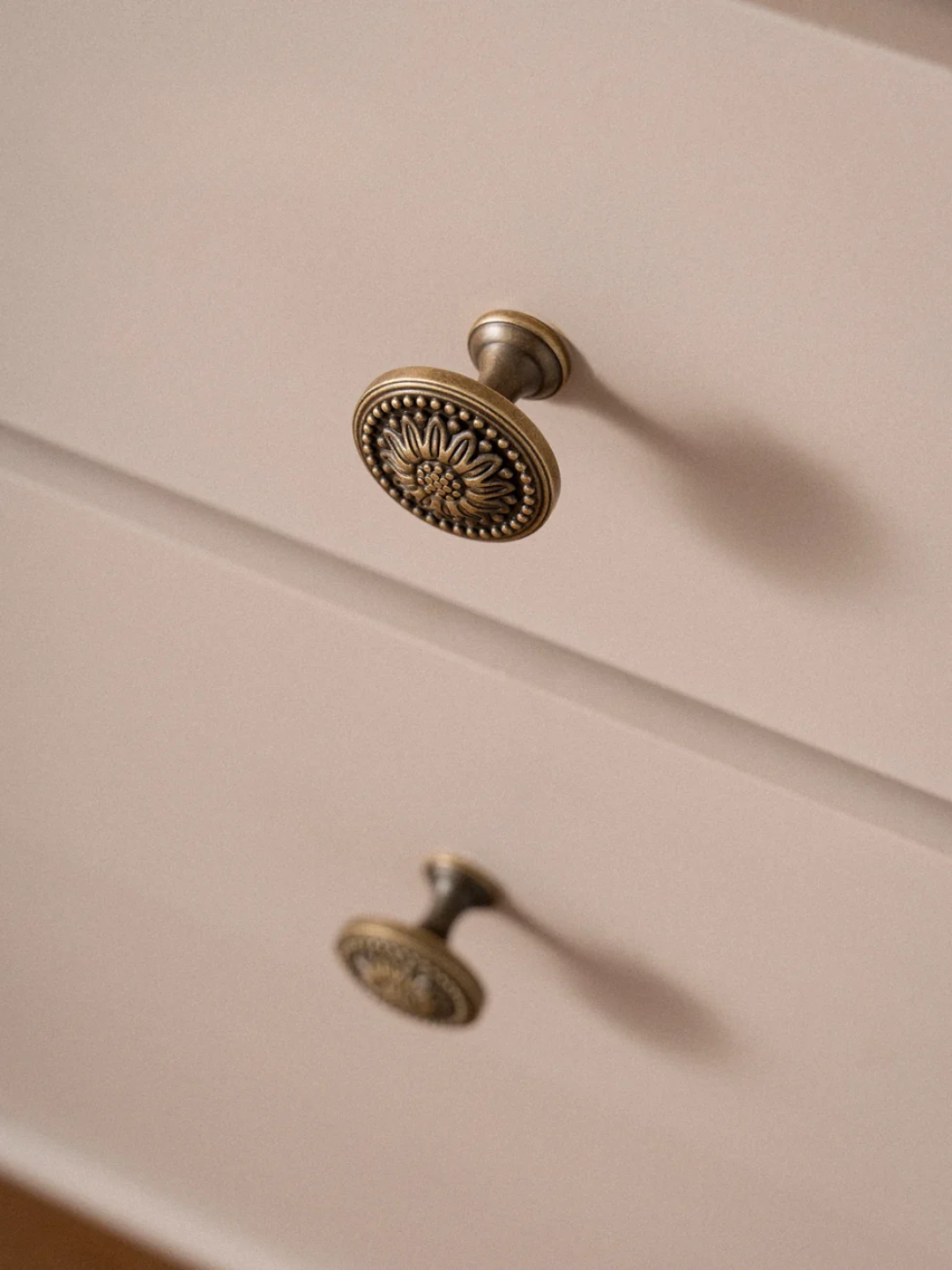 Close-up of a decorative brass cabinet knob on a wooden drawer.