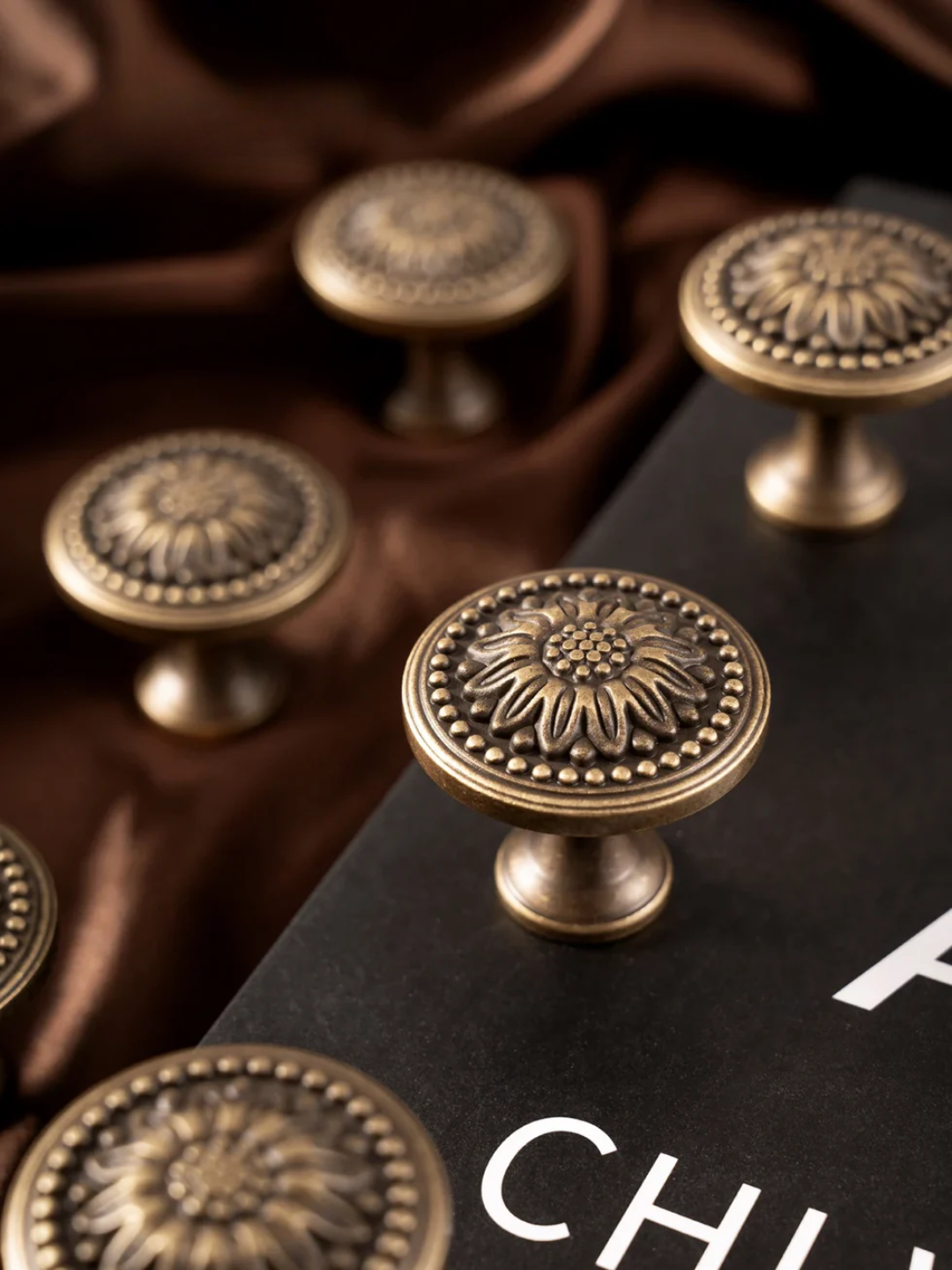 Bronze cabinet knobs on a dark surface with 'CHU' visible