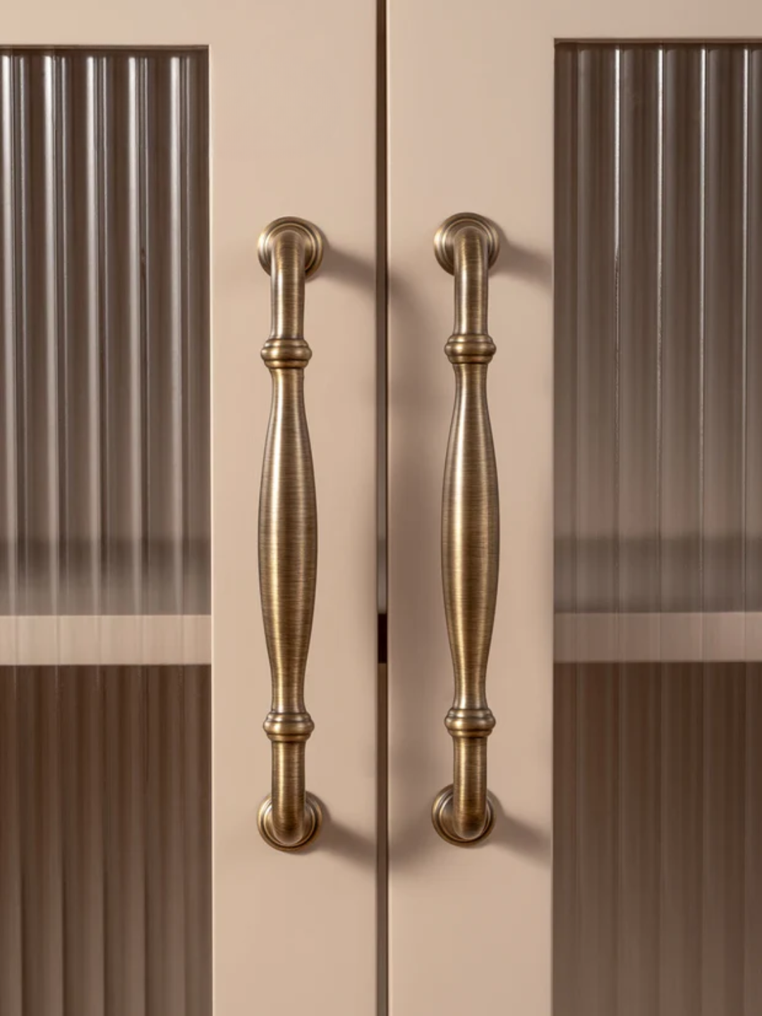 Close-up of a pair of bronze cabinet handles on a beige background