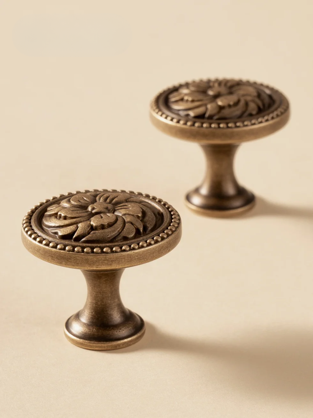Two ornate bronze cabinet knobs on a beige background