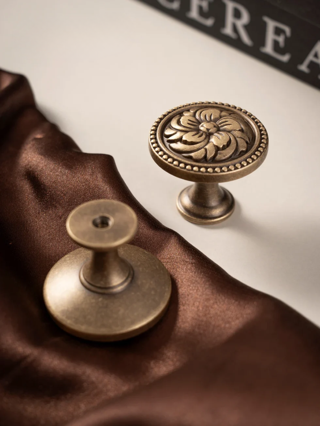 Two brass cabinet knobs on a brown fabric background