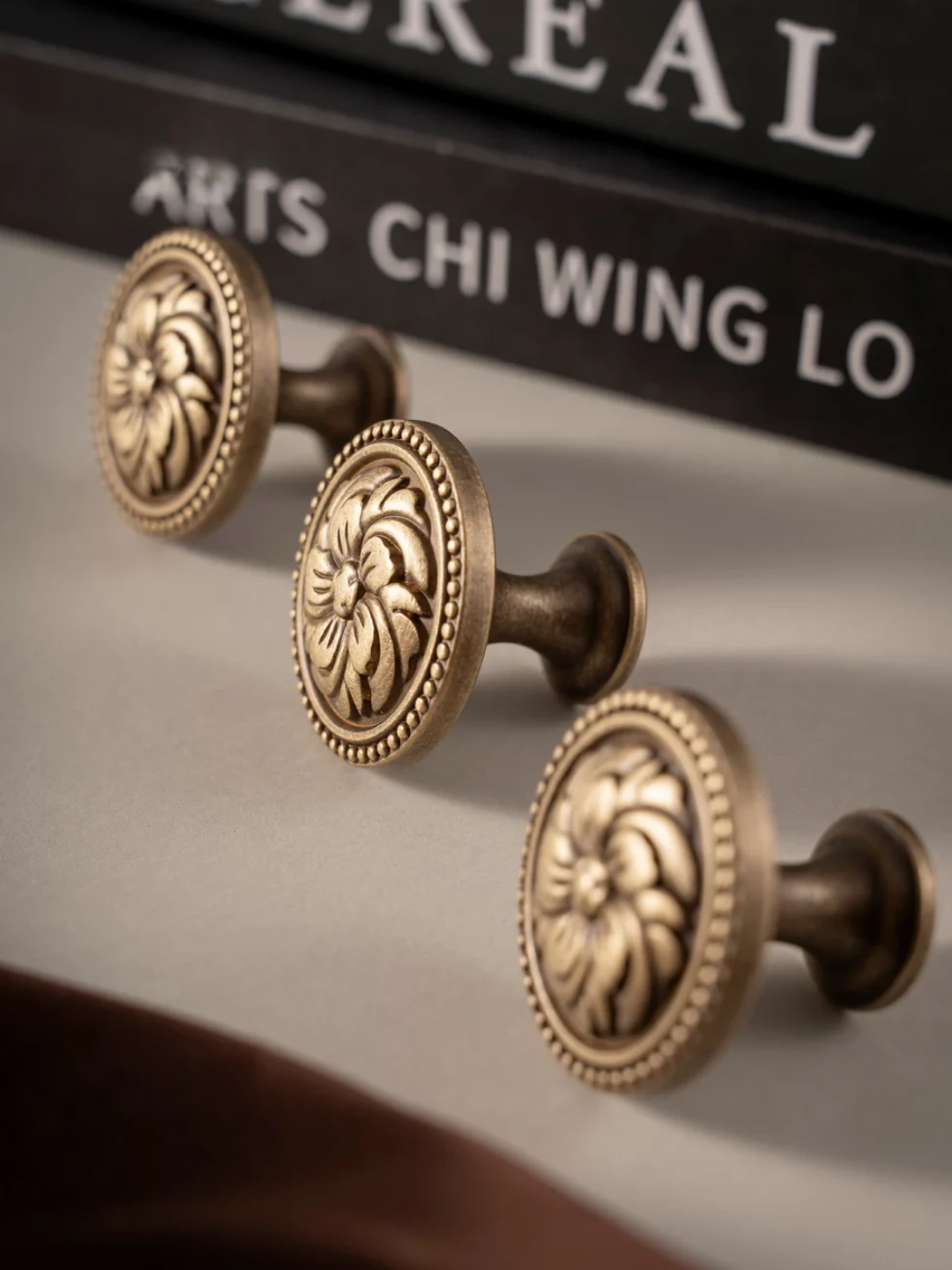 Three ornate bronze cabinet knobs on a book with text in the background