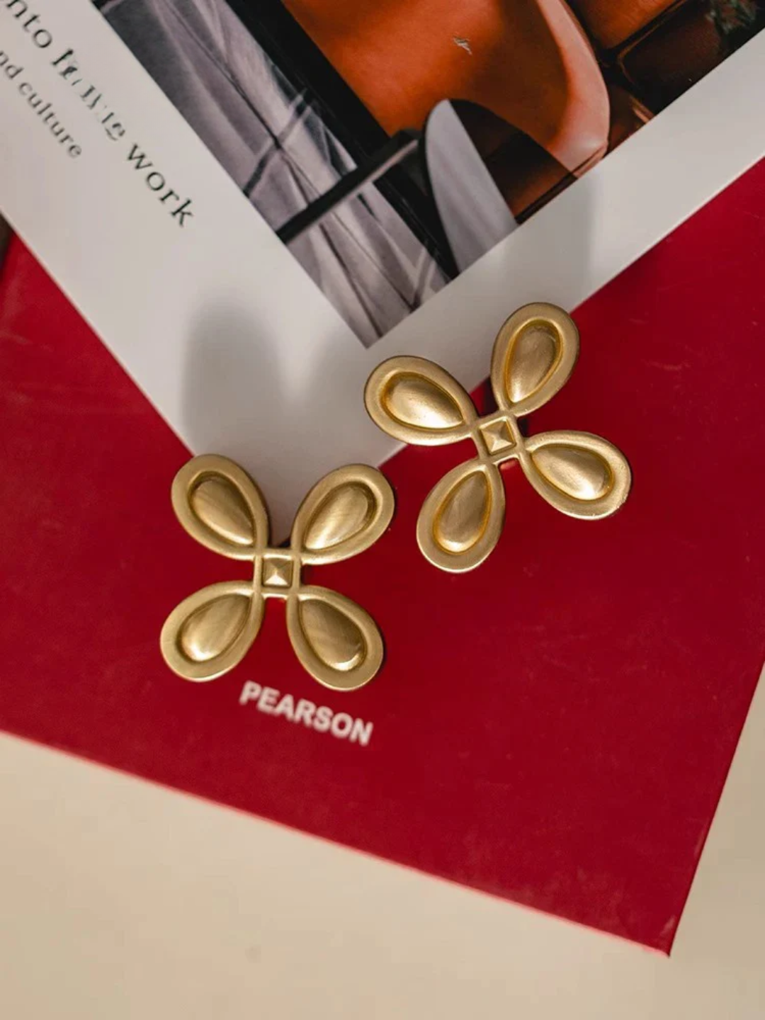 Gold bow-shaped earrings on a red Pearson book cover