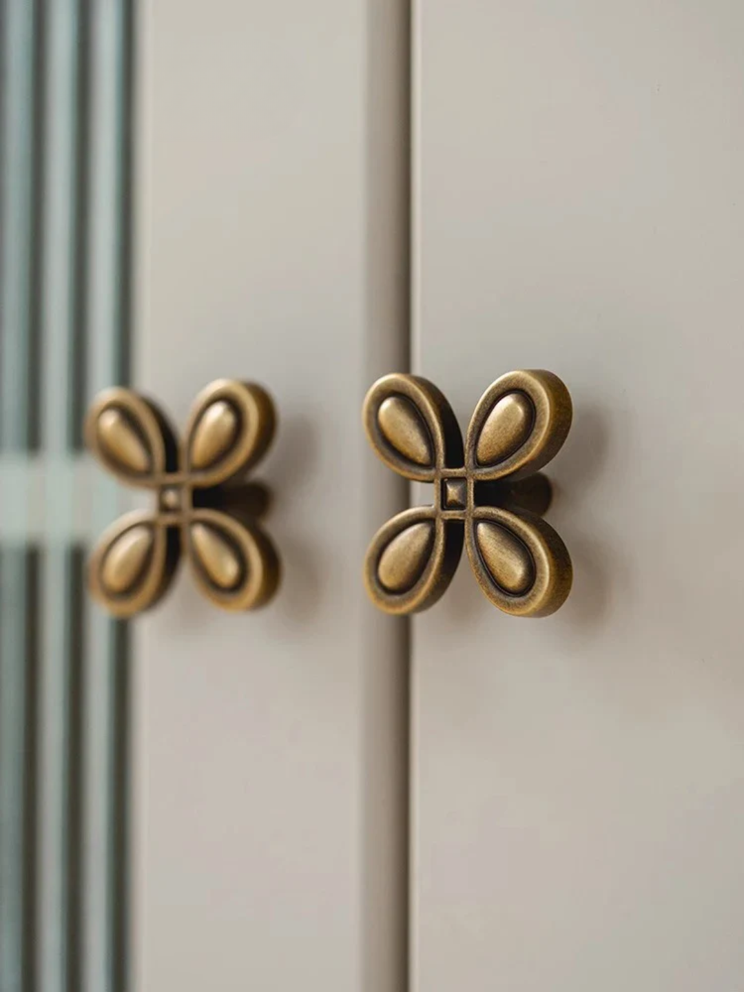 Close-up of two gold butterfly-shaped cabinet knobs on a light-colored cabinet door.