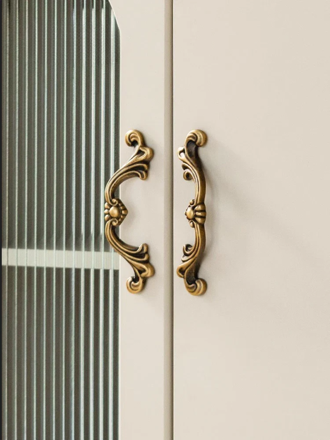 Decorative gold handles on a white cabinet with glass panel