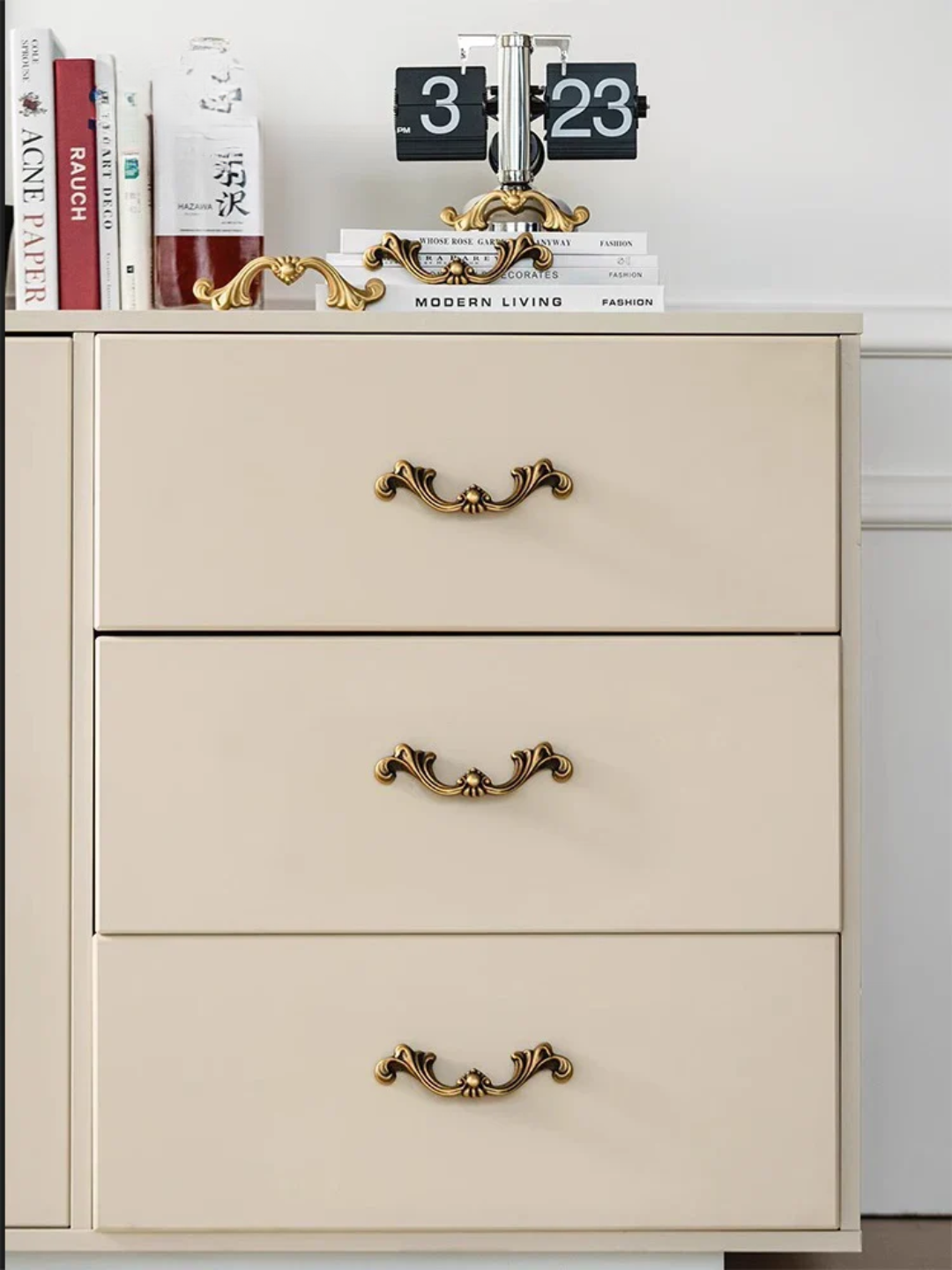 Beige dresser with gold handles and books on top against a white wall.