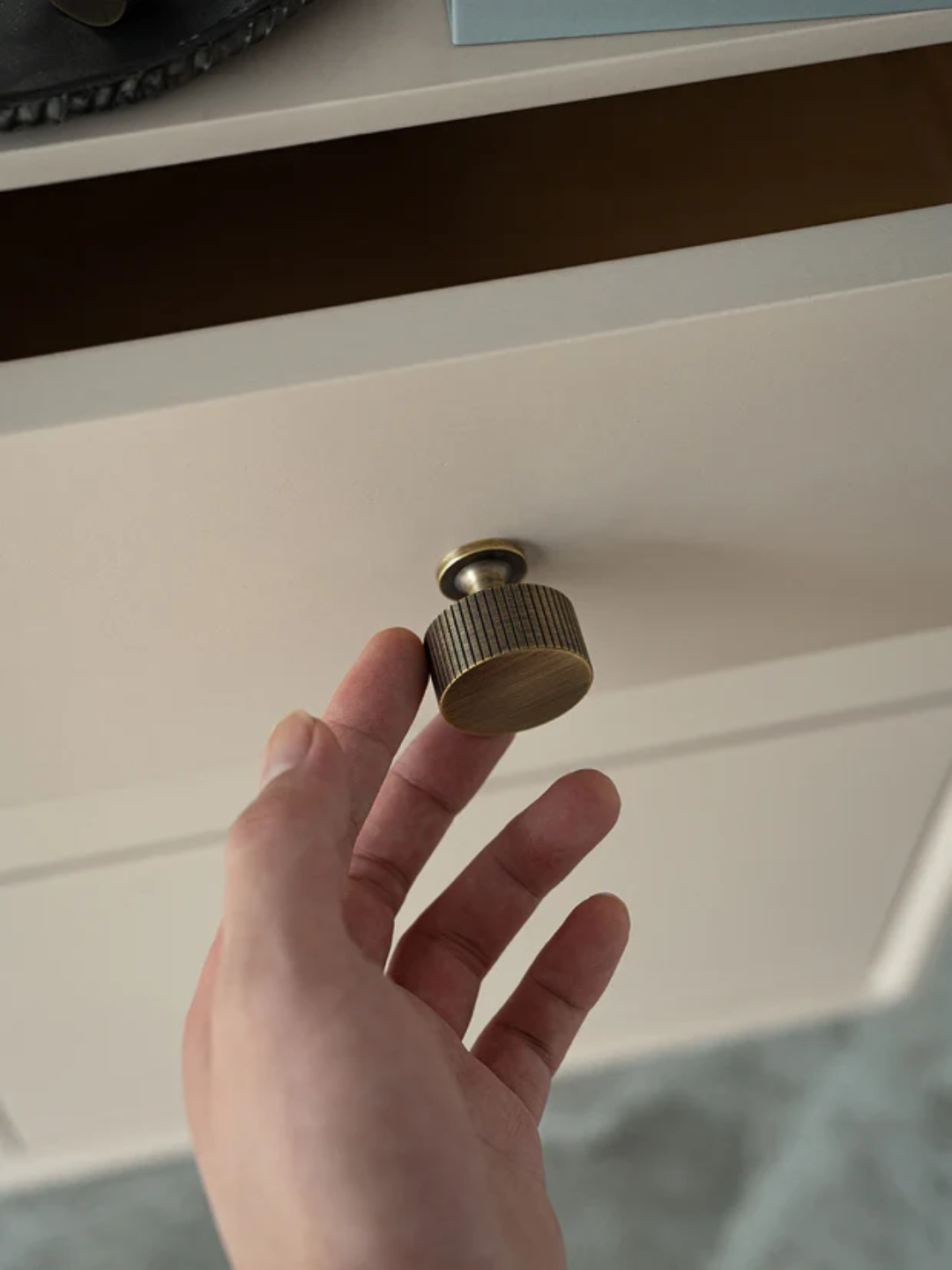 Hand holding a brass knob above a white cabinet