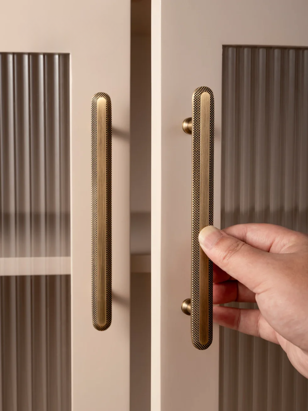 Hand opening a door with gold handles on a neutral background