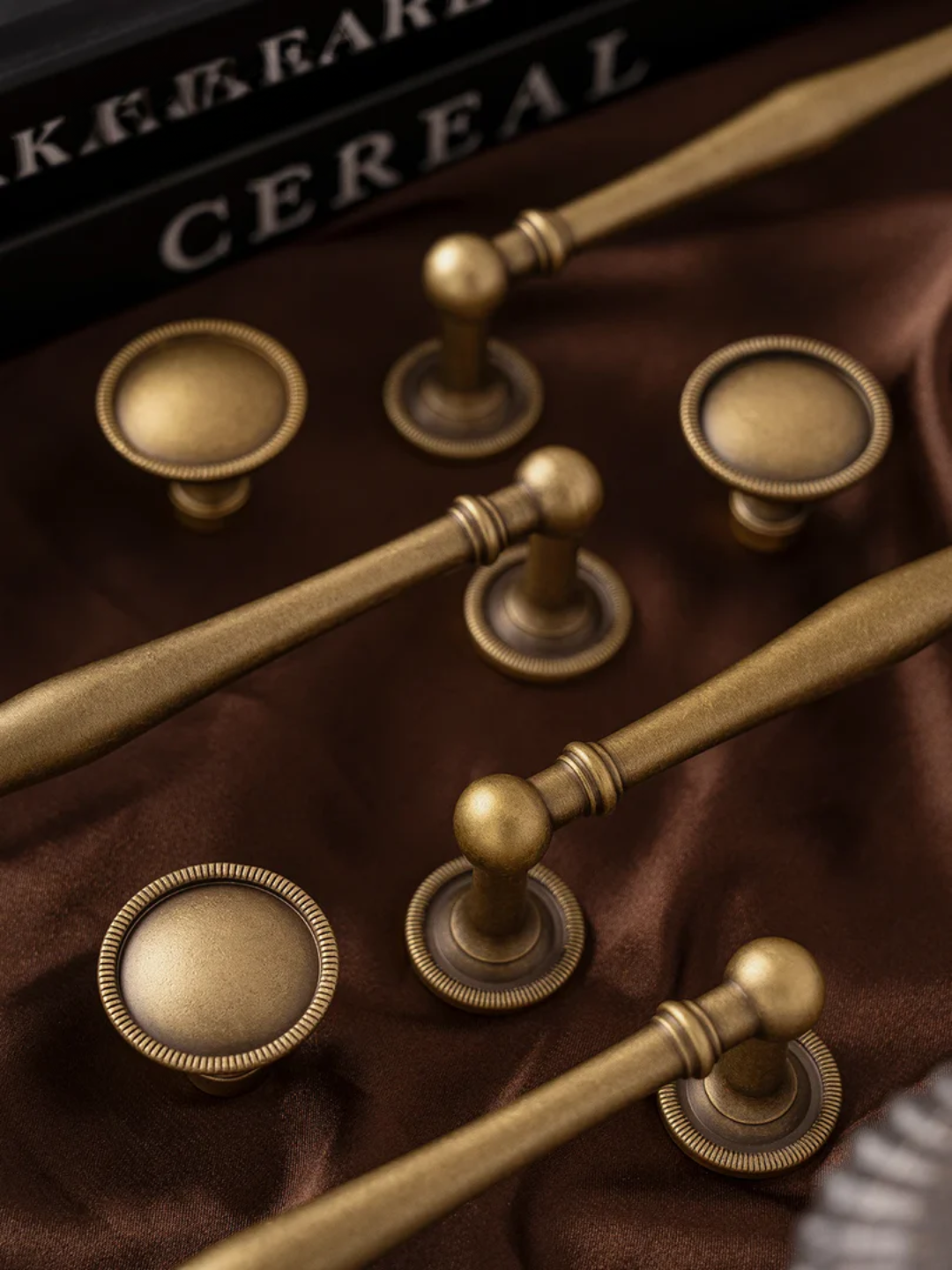Set of gold cabinet handles on a brown surface with 'Shakespeare Cereal' book in the background.