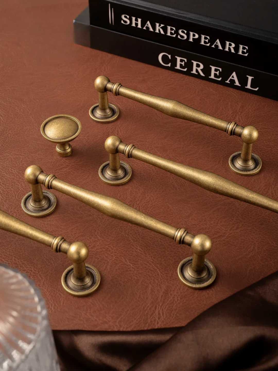 Set of gold cabinet handles on a brown surface with 'Shakespeare Cereal' book in the background.