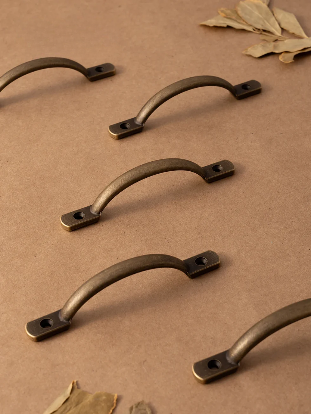 Set of bronze cabinet handles on a brown surface with leaves.