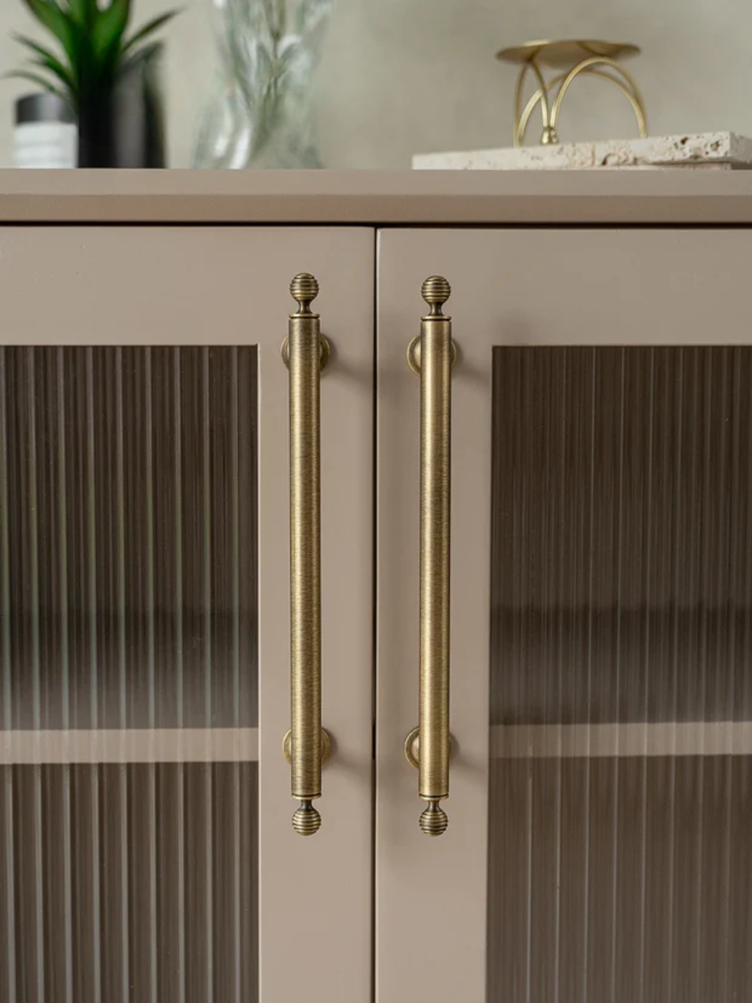 Cabinet with gold handles and glass doors in a neutral setting