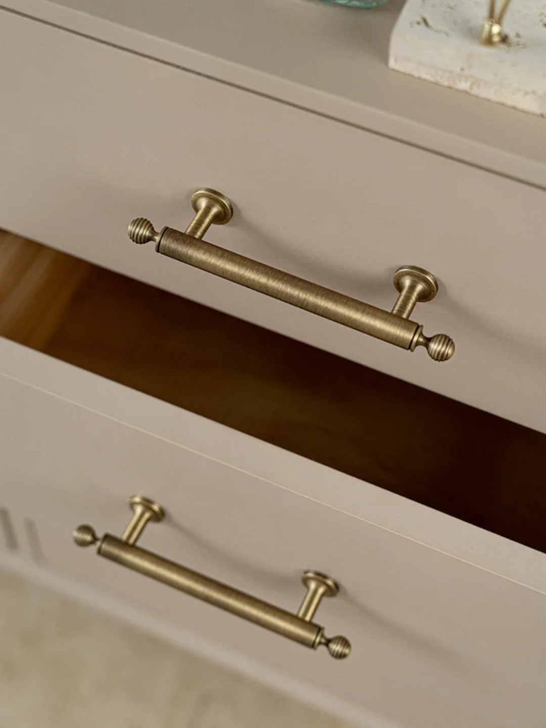 Close-up of a beige drawer with gold handles on a wooden floor.