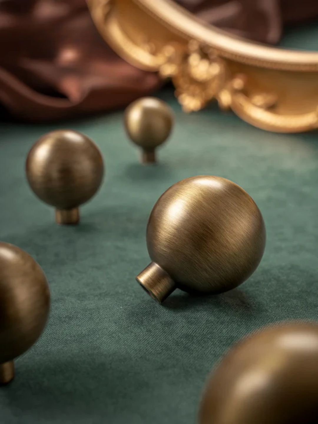 Bronze knobs on a green surface with a decorative gold object in the background