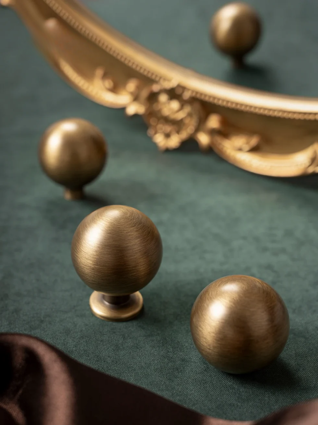 Bronze knobs on a green surface with a decorative mirror in the background