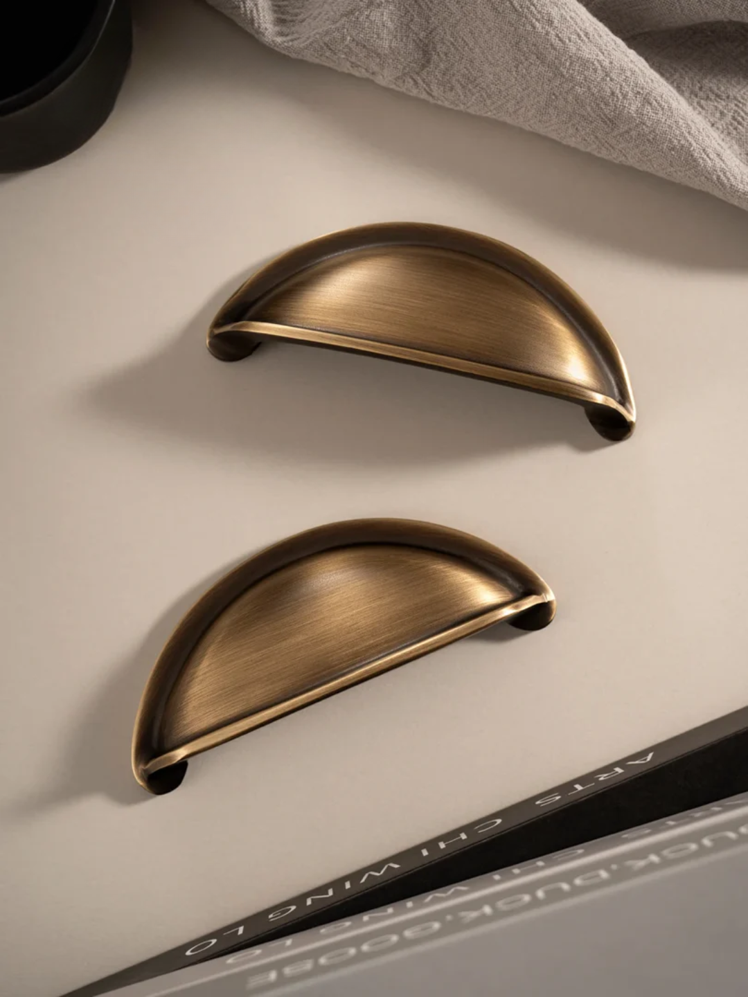 Two bronze cabinet handles on a light surface with a pen and paper in the background.