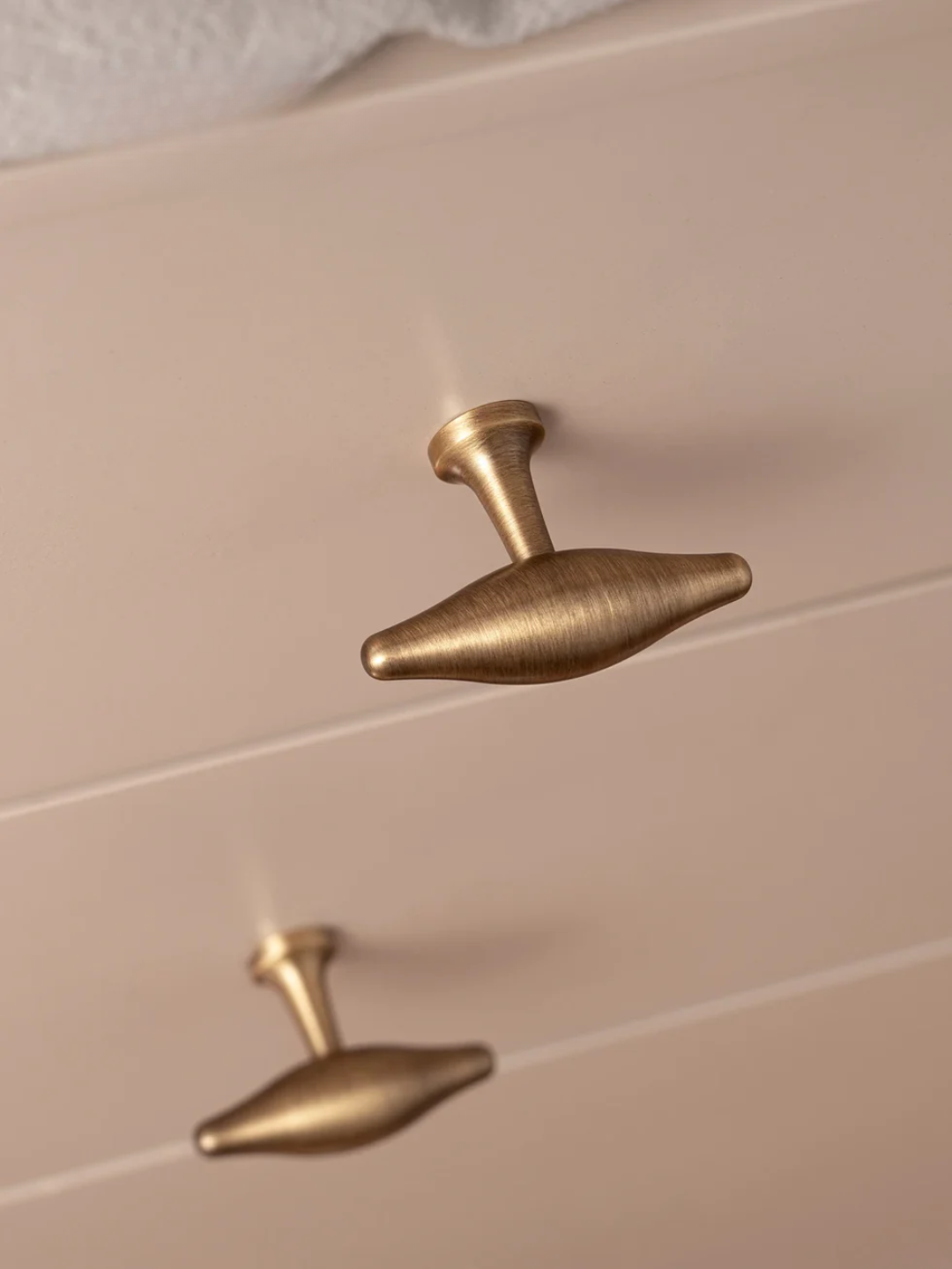 Two gold cabinet knobs on a beige cabinet door.