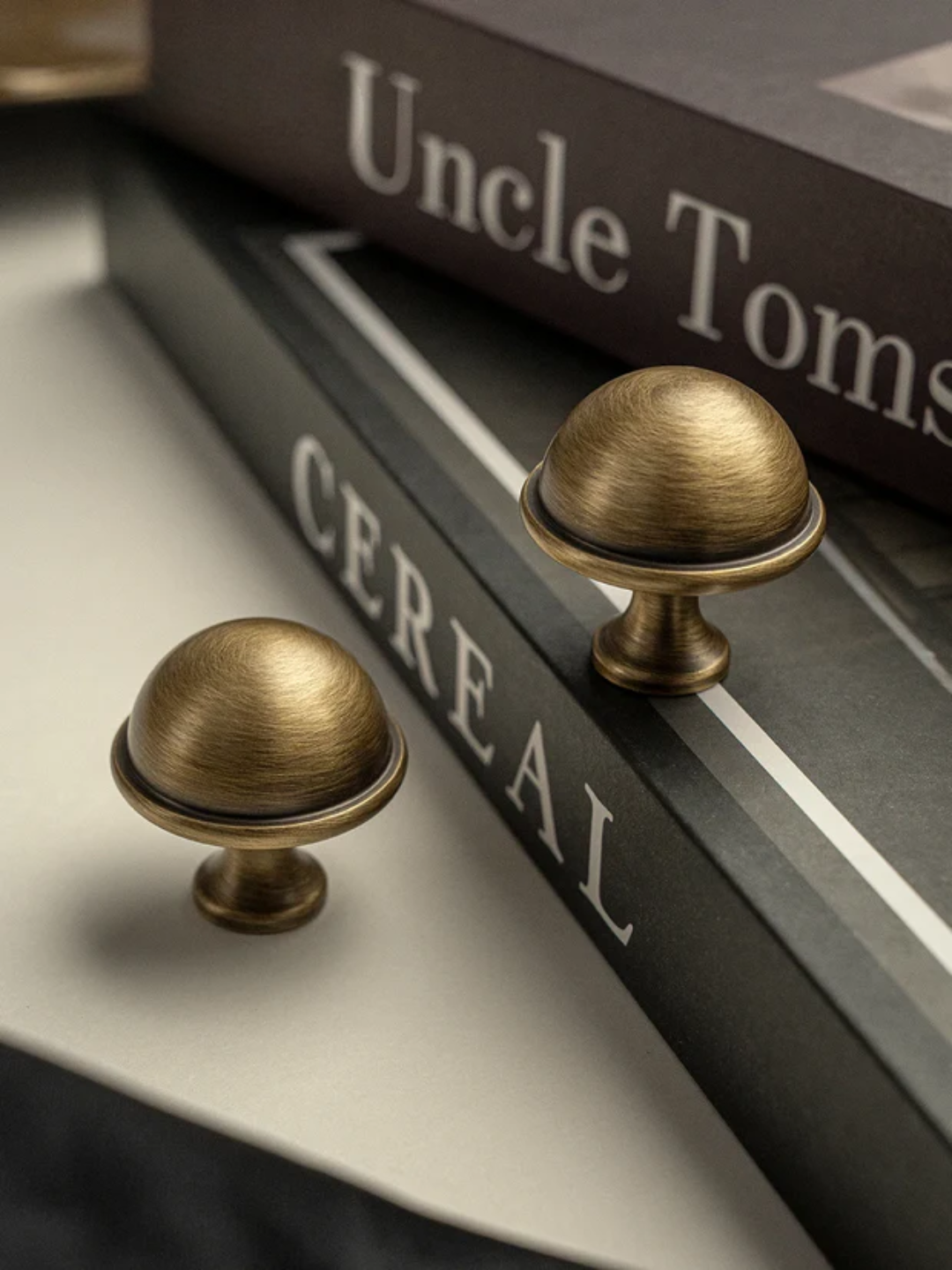 Two brass cabinet knobs on a book titled 'Uncle Tom's Cabin' with 'CEREAL' visible.