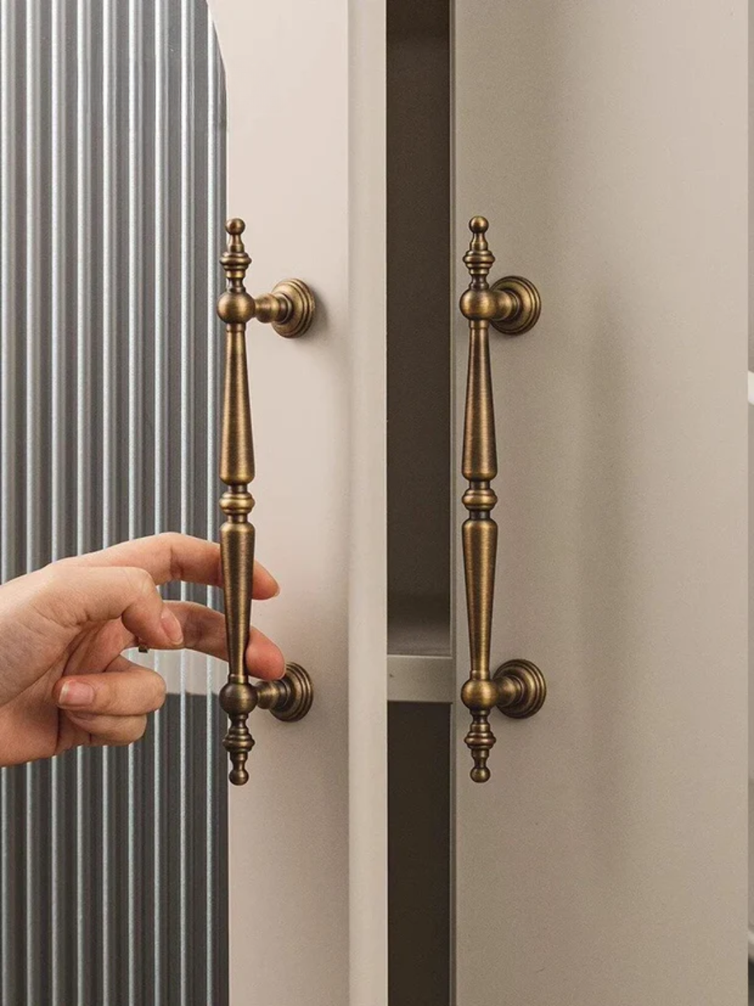 Hand opening a door with ornate brass handles.