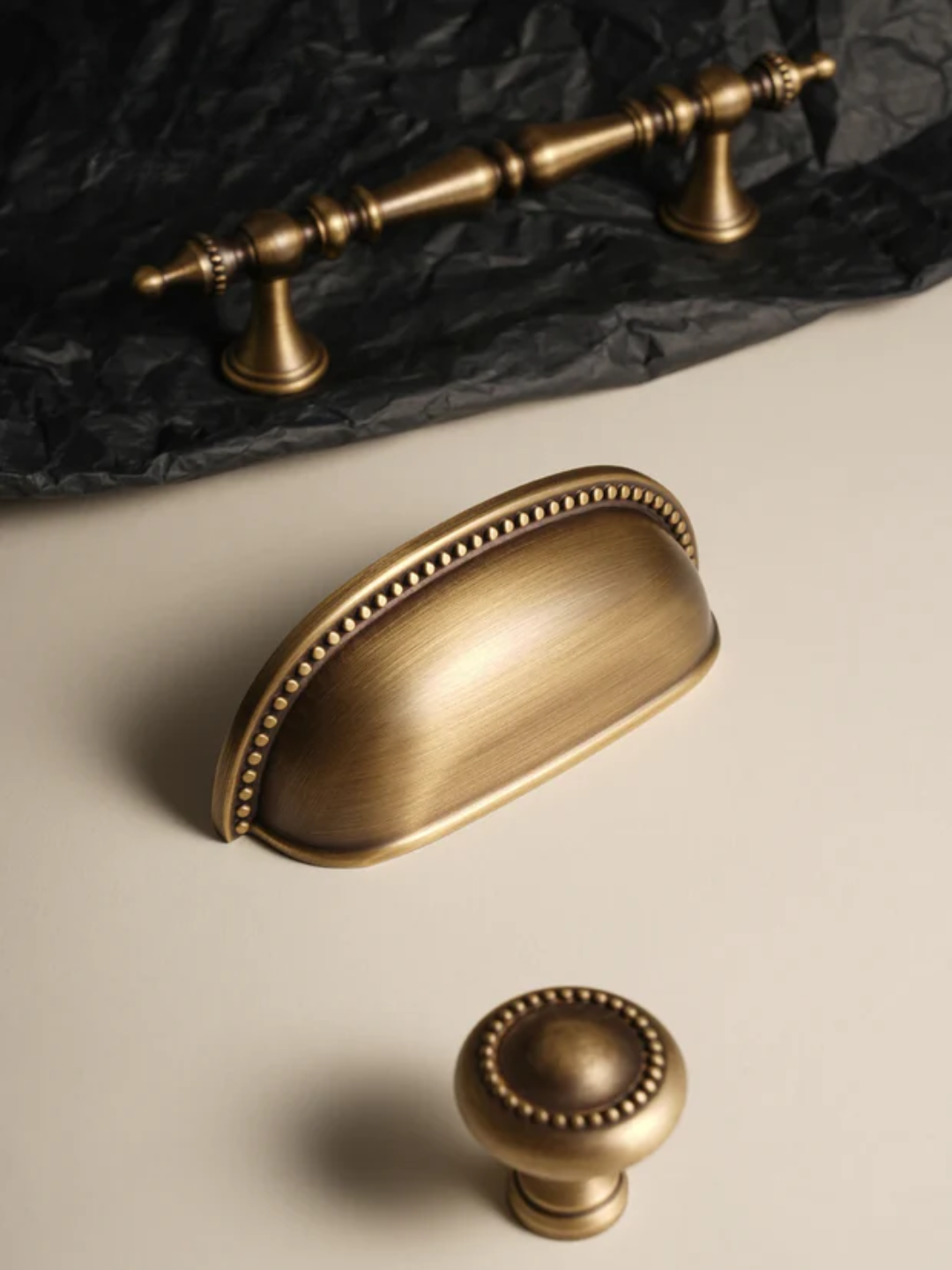 Set of gold cabinet handles on a beige surface with black fabric background