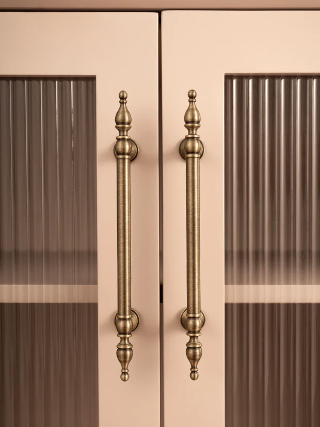Close-up of a pair of ornate bronze cabinet handles on a beige background