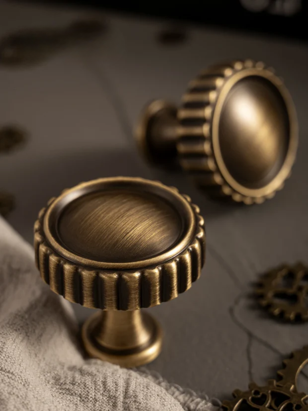 Two bronze cabinet knobs on a textured surface with gears in the background