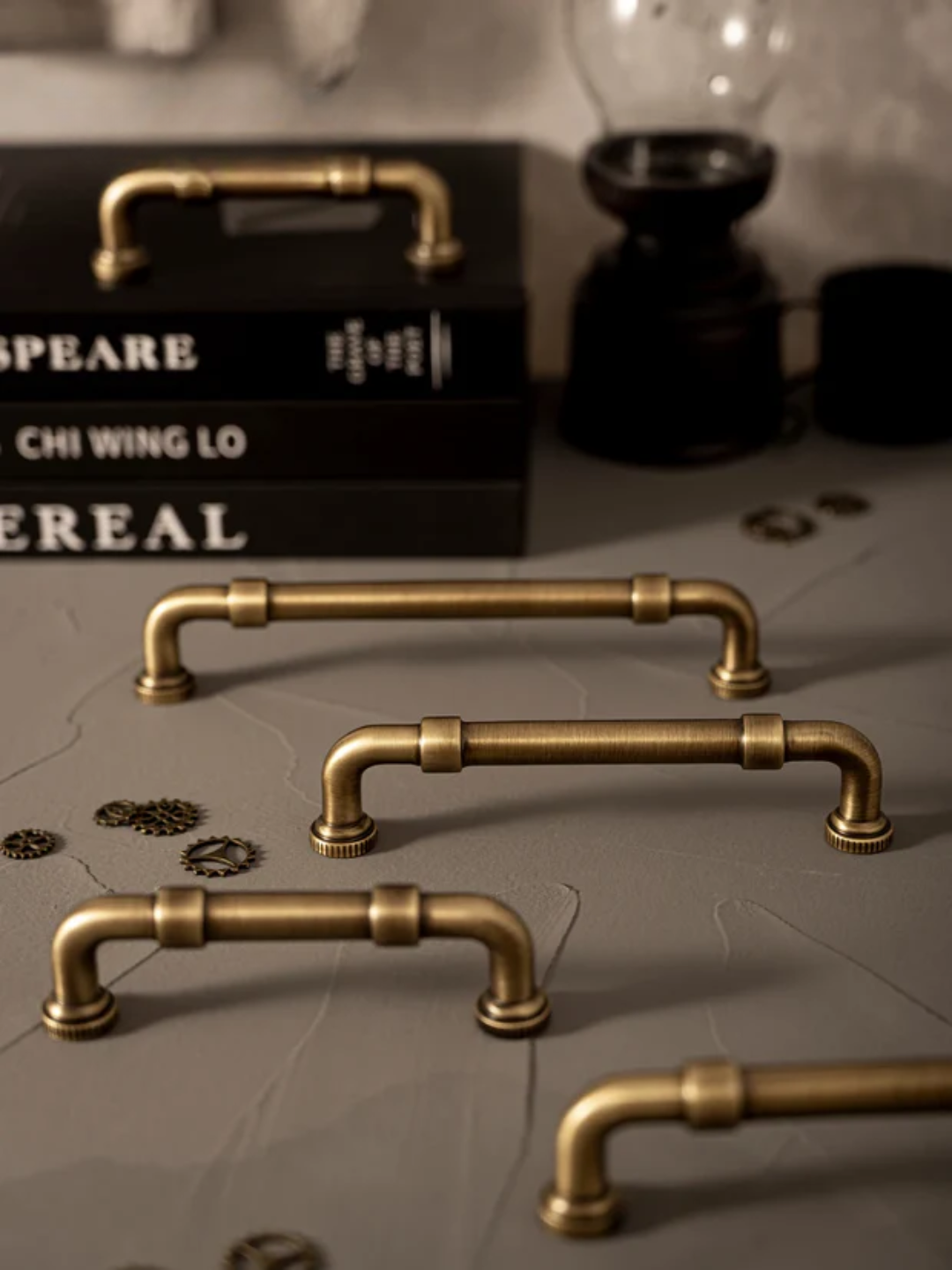 Set of gold pipe-style cabinet handles on a textured surface with books in the background.